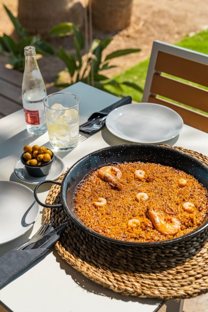 A delicious seafood paella served on an outdoor table with a bottle of water and a glass of ice.